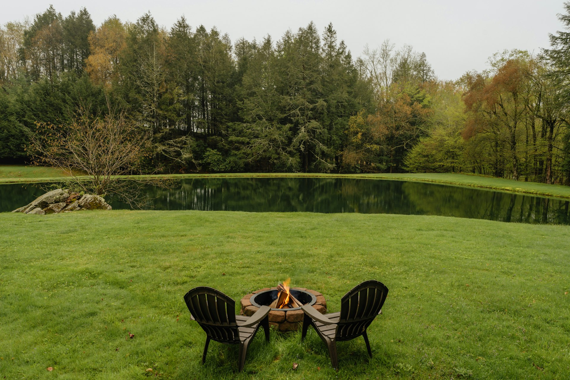 Two chairs sit around a fire by a lake.